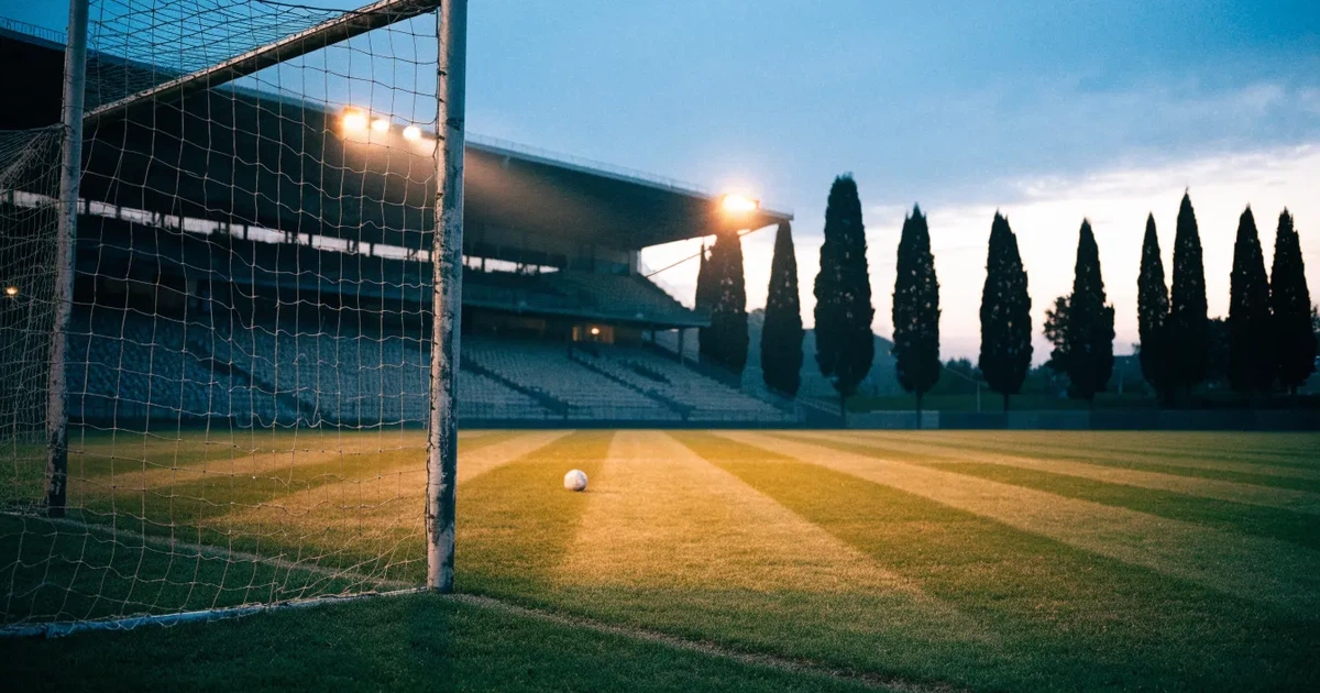 Ein Fußballtor mit Netz auf einem leeren Platz im Abendlicht, der Rasen frisch gemäht, im Hintergrund Zypressen.