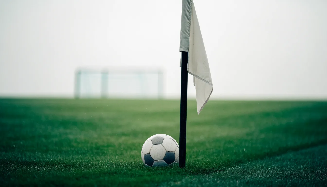 Ein Fußball liegt neben einer Eckfahne auf kurz gemähtem Rasen unter bewölktem Himmel.